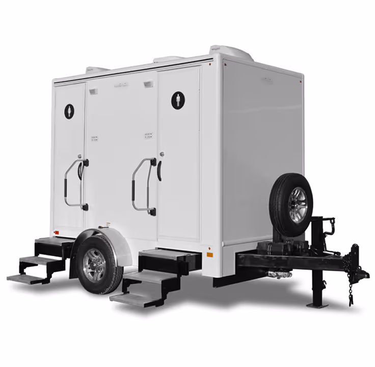 Two-door white portable restroom trailer with steps and handrails on each entrance, spare tire attached to front trailer hitch
