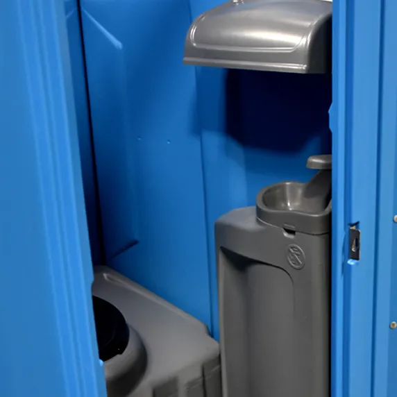 Interior of blue portable restroom showing handwash station and toilet seat with lid