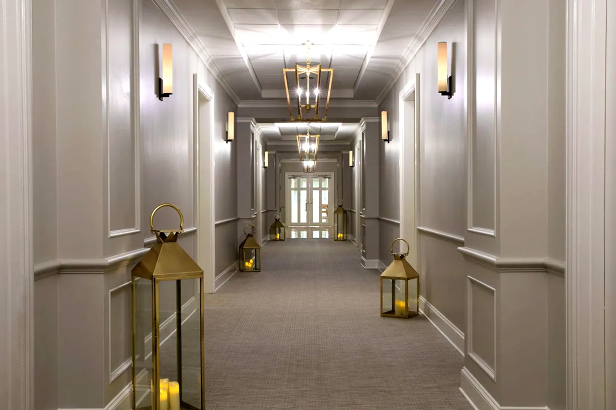 Hotel hallway with gray walls, brass lanterns with candles on the floor, and modern ceiling lights