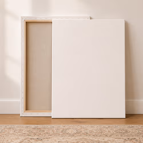 Two blank white canvases leaning against a beige wall on a wood floor with a rug in front.