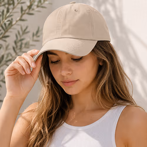 Young woman with long hair wearing a beige hat and white tank top, touching the hat's brim.