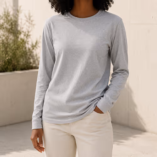 Woman wearing a light gray long-sleeve shirt and beige pants standing outdoors with one hand in pocket.