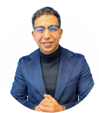 Smiling man with glasses wearing a blue blazer and black turtleneck against white background.