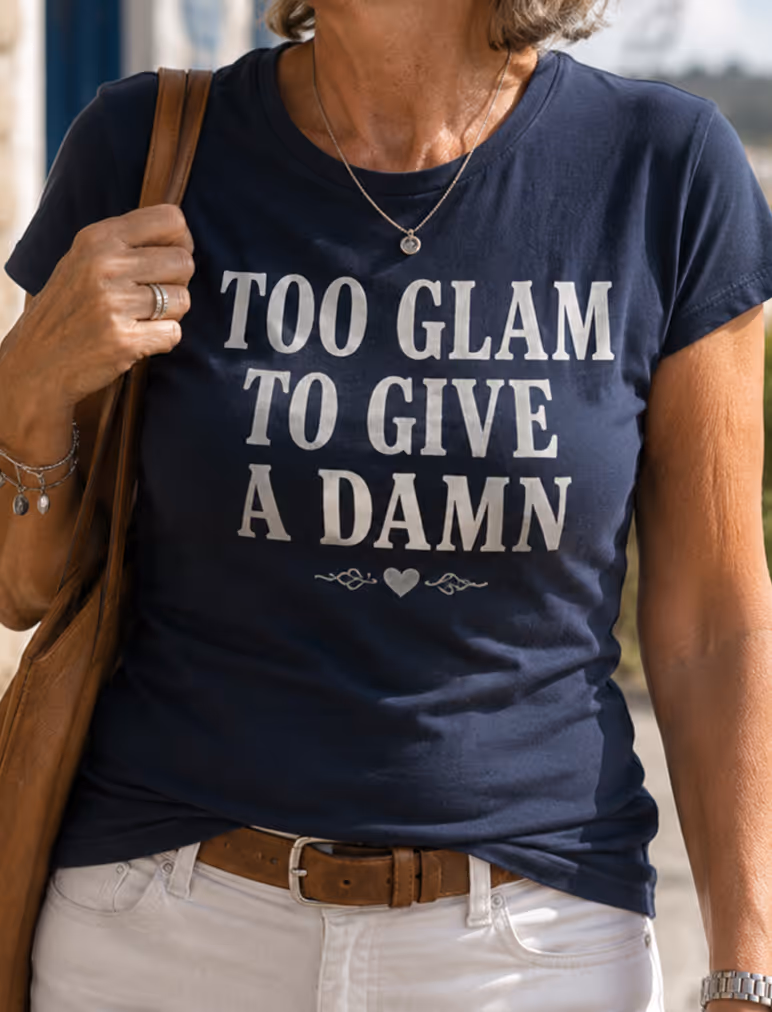 Woman wearing navy shirt with white text, 'TOO GLAM TO GIVE A DAMN', brown belt, and white pants.