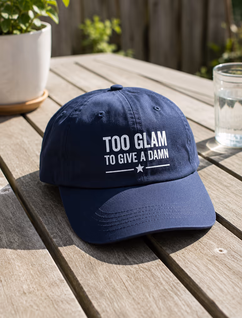 Navy blue cap on wooden table with white text: 'TOO GLAM TO GIVE A DAMN'.
