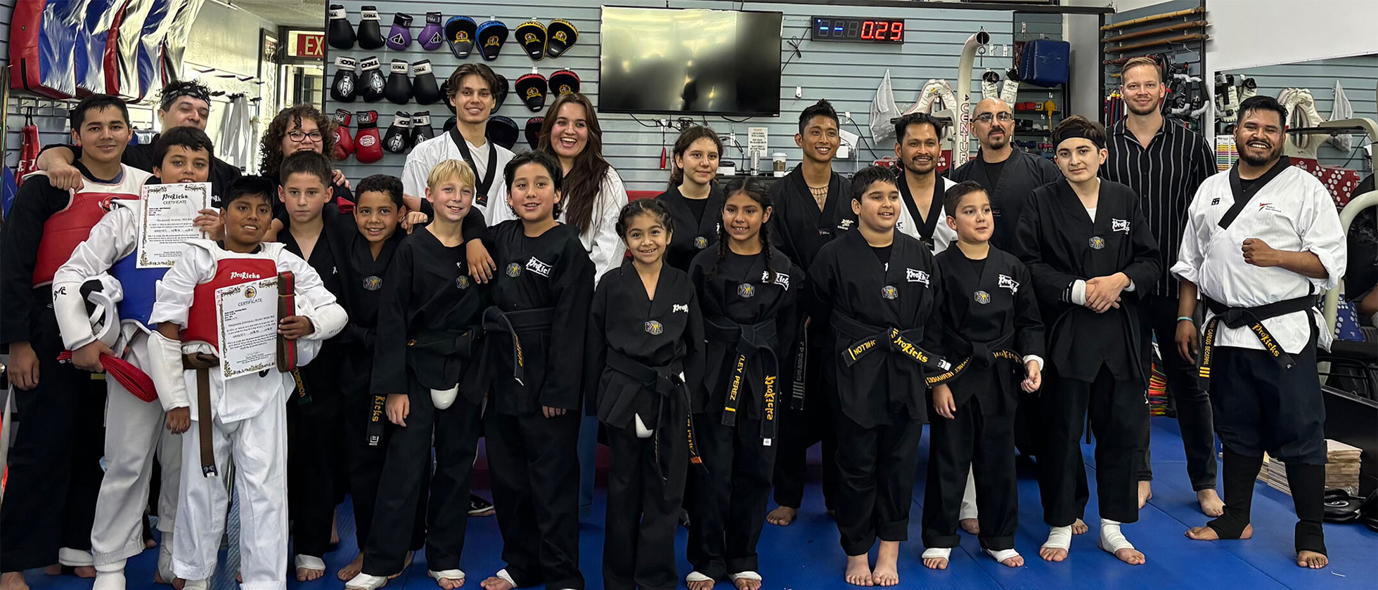 Group of martial arts students and instructors in black and white uniforms posing inside a gym.