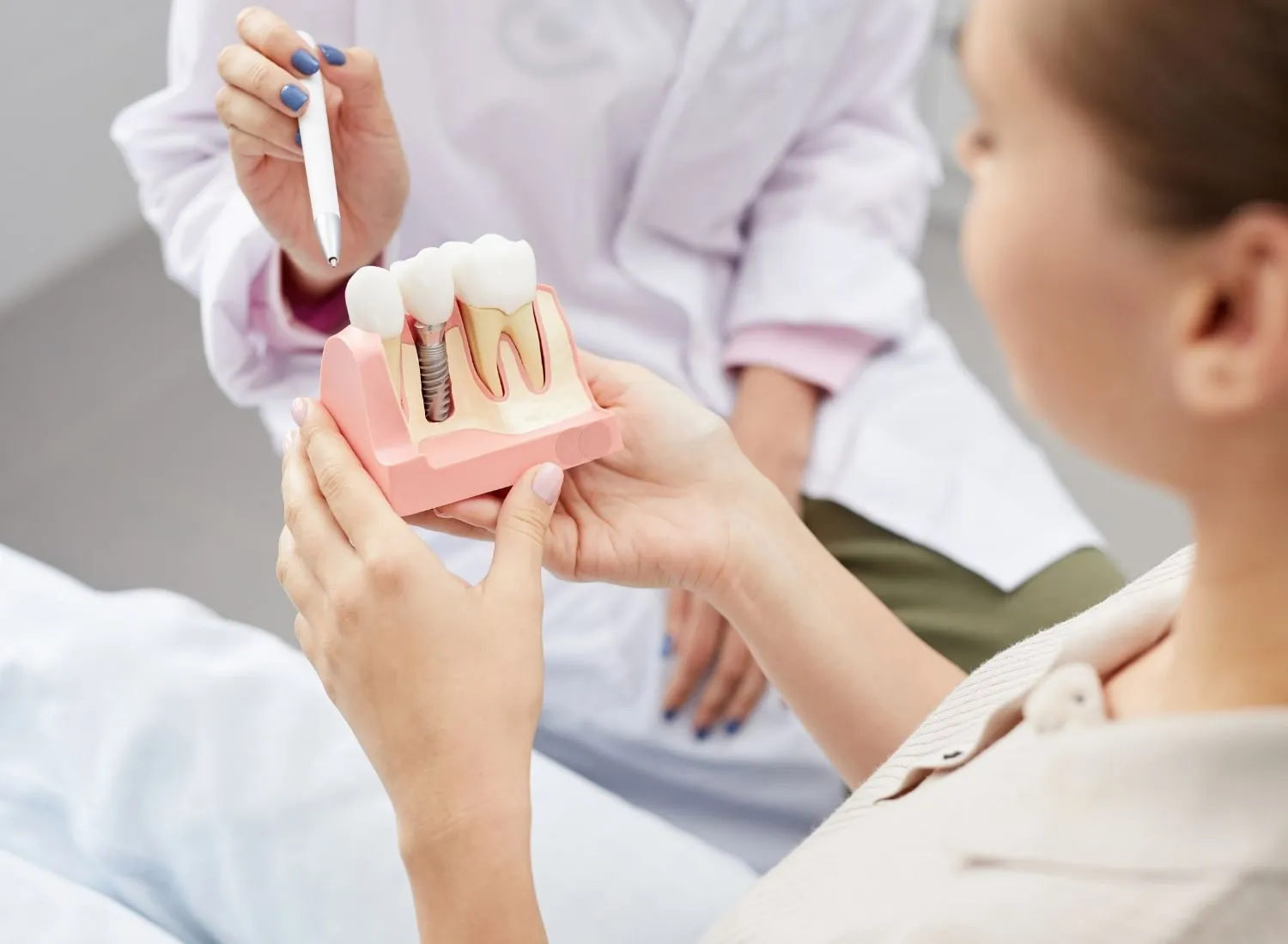 Dentist showing a patient a dental model with natural teeth and a dental implant.