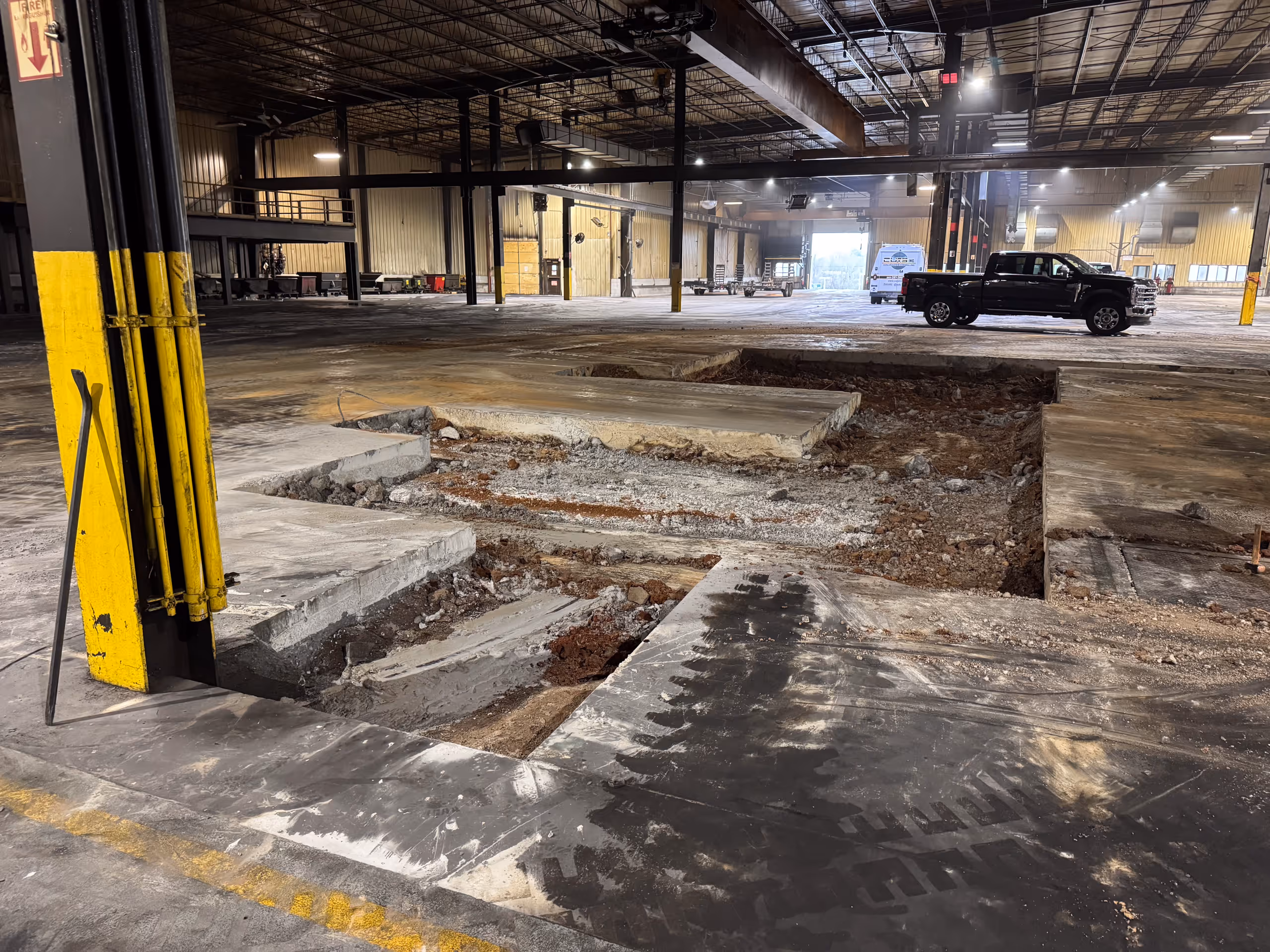 Large industrial warehouse with exposed concrete floor sections and a black pickup truck inside.