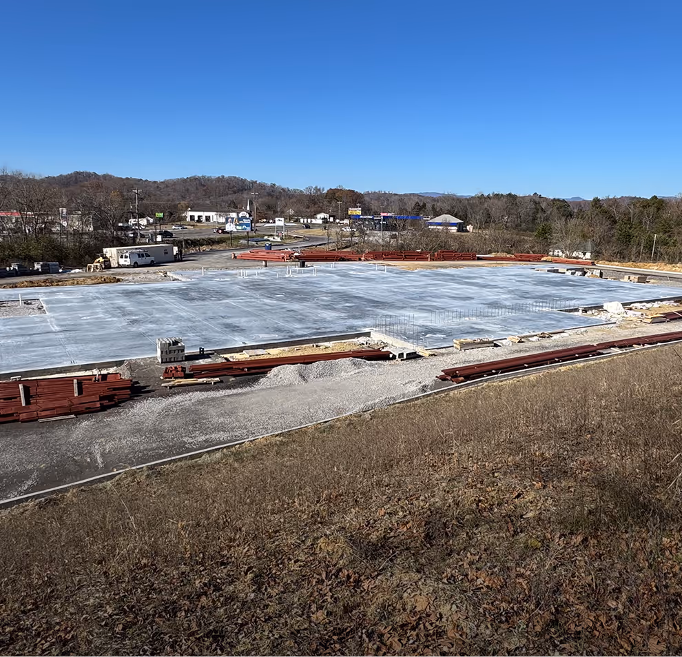 Concrete foundation slab at a construction site with building materials nearby and a clear blue sky.