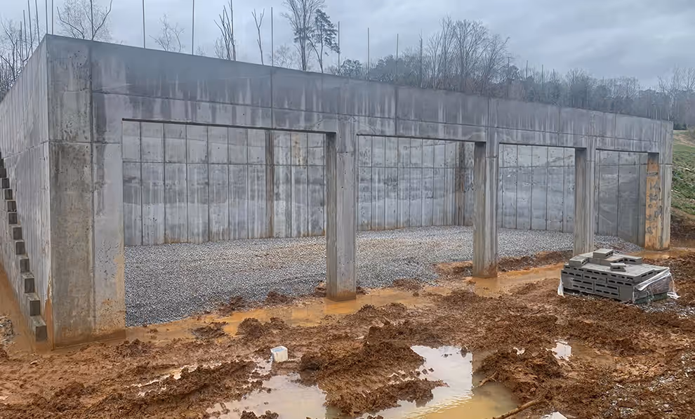 Concrete foundation structure at a muddy construction site with gravel inside and pallet of concrete blocks.