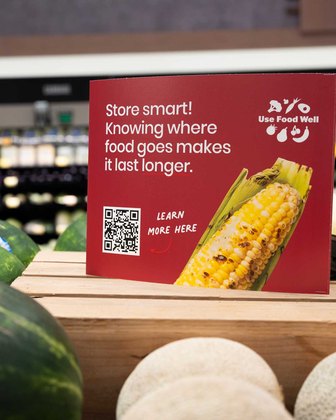 Red Use Food Well sign in a grocery store produce section reading Store smart! Knowing where food goes makes it last longer, with a QR code