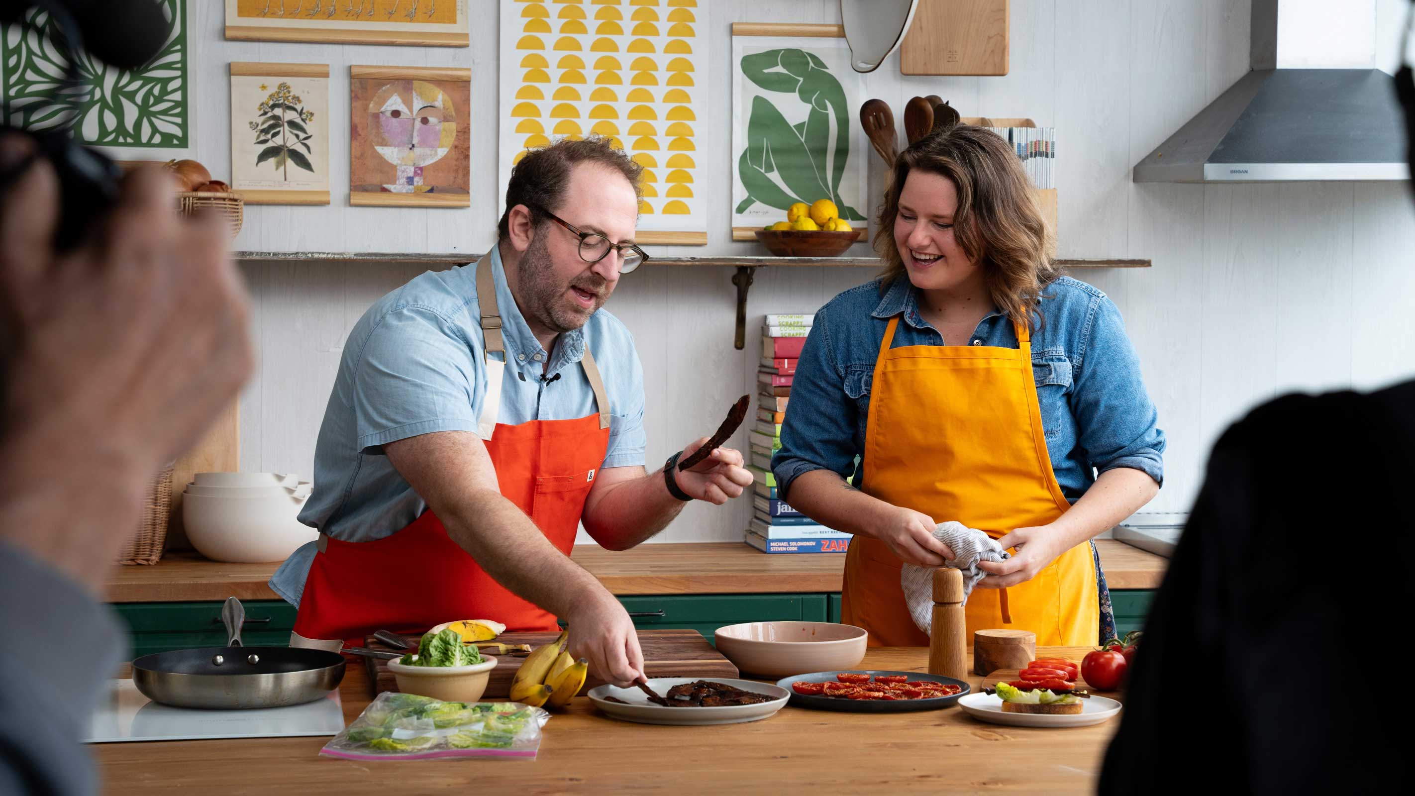 Two cooks in aprons preparing food on camera in a bright kitchen studio during a video shoot