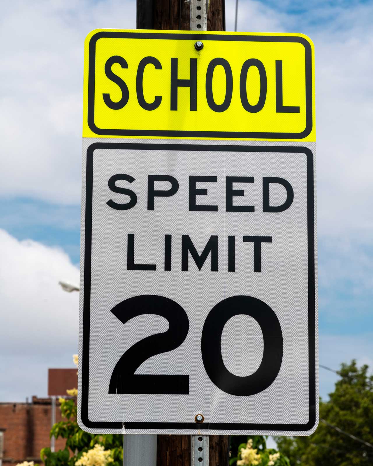 A road sign in a school zone posting a 20 mile per hour speed limit against a blue sky