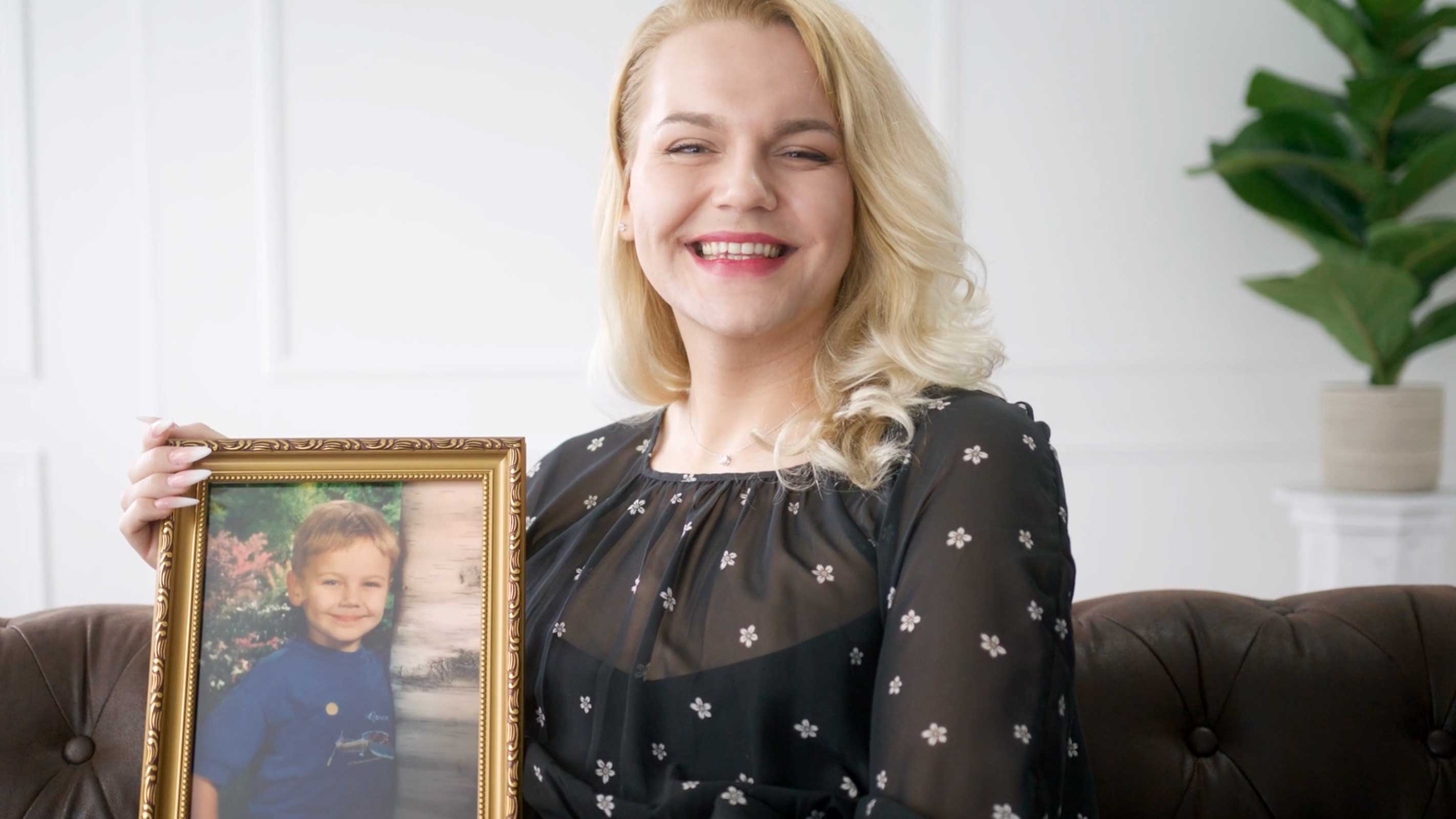 A smiling LGBTQIA+ Washington resident holds a framed photo of herself as a child