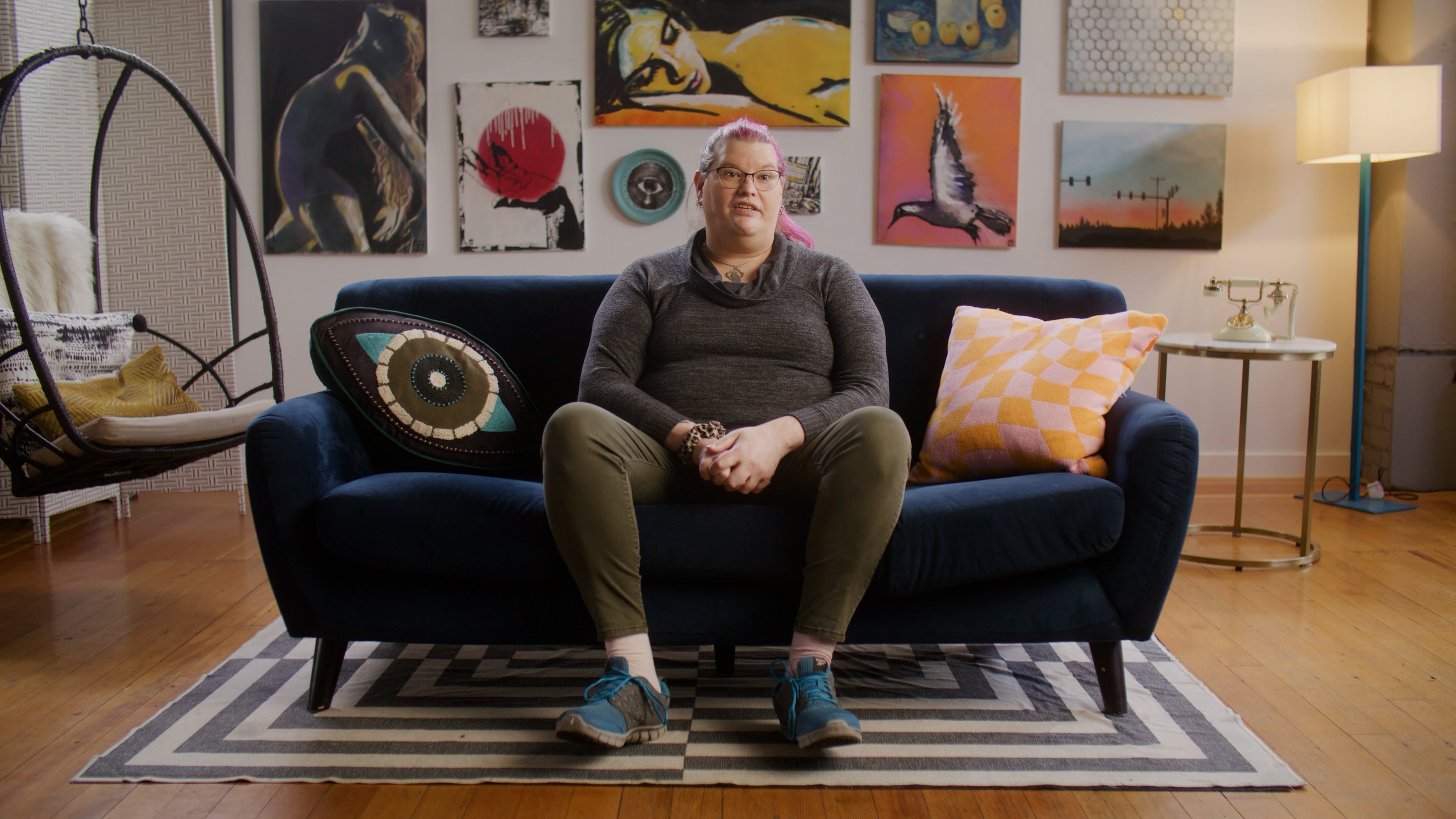Community storyteller Carrie sits on a blue couch in a room filled with colorful art