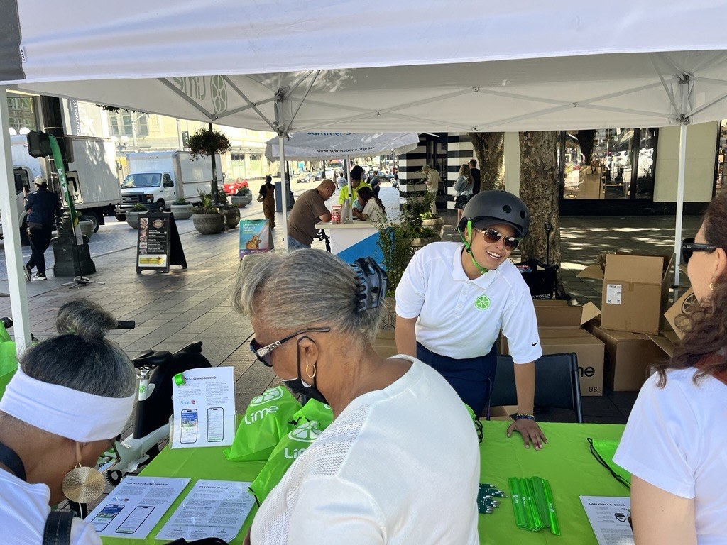 A Lime brand ambassador wearing a helmet talks with community members at a Lime outreach tent in downtown Seattle