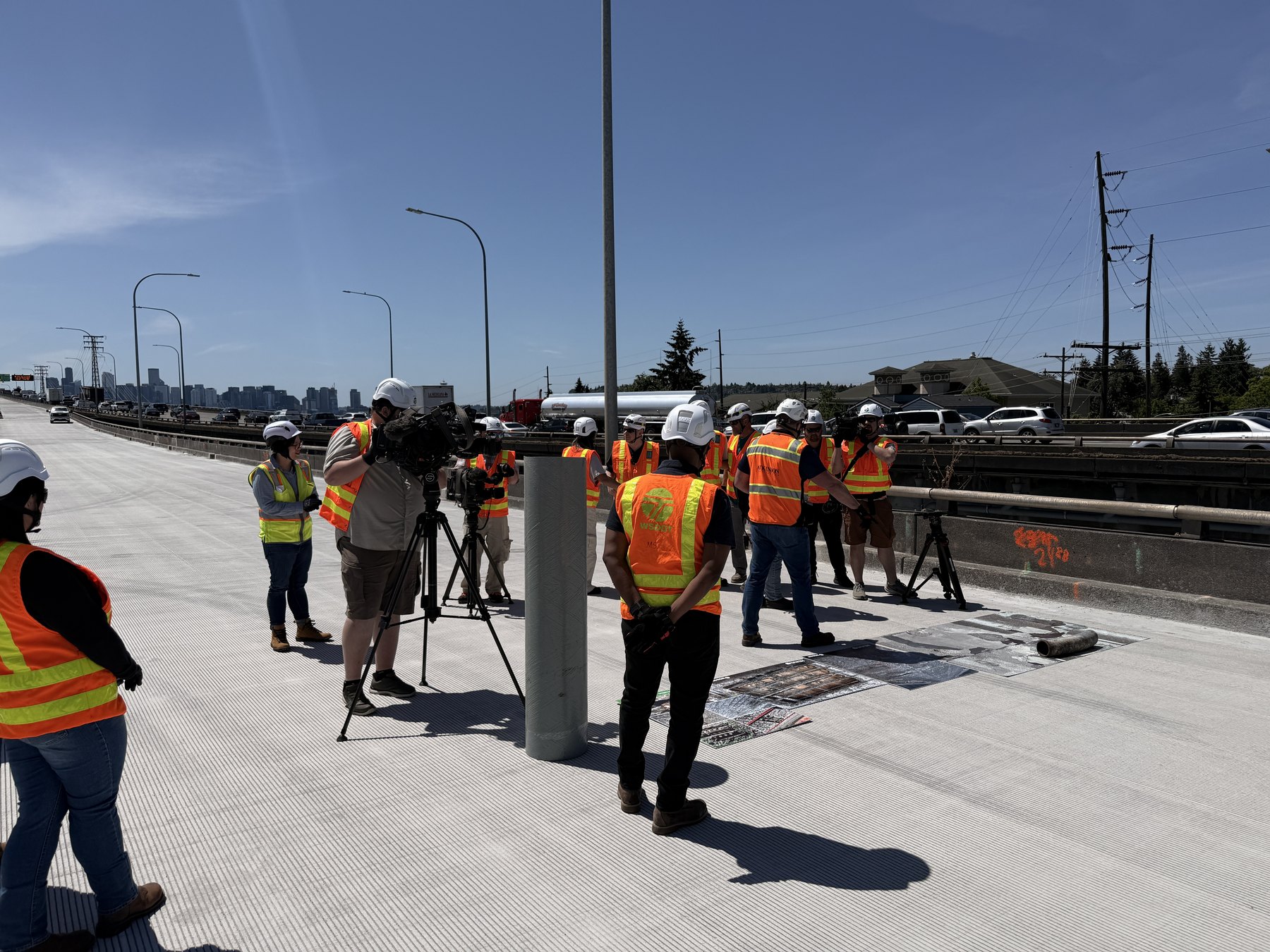 Television crews and WSDOT staff in safety vests gather for a media event on the newly resurfaced bridge deck