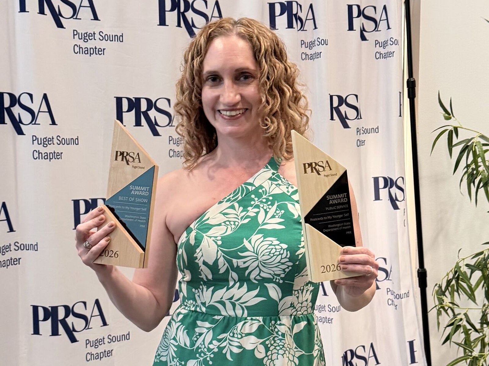 A PRR team member holding the 2026 PRSA Puget Sound Summit Awards for Best of Show and Public Service in front of a PRSA Puget Sound Chapter backdrop.
