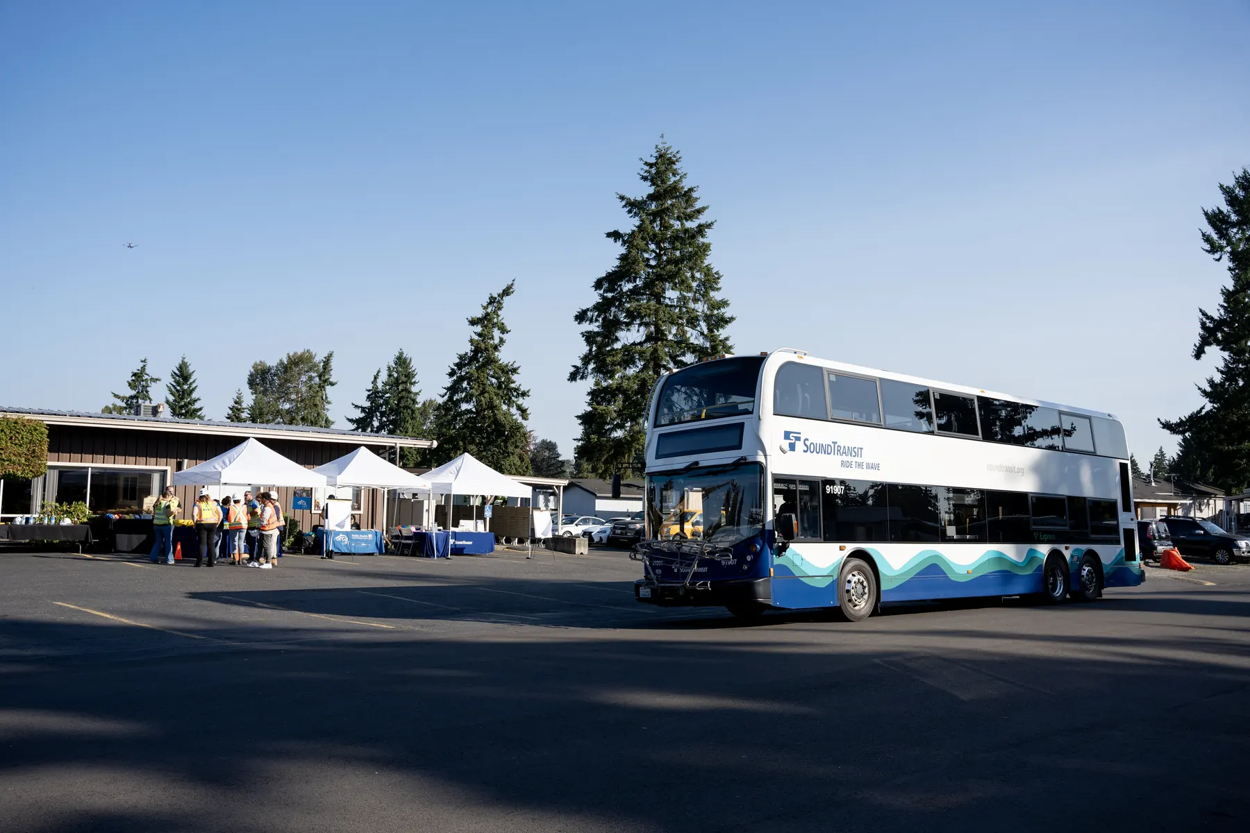 A Sound Transit double-decker bus parked beside the community outreach tents at a Federal Way Link Extension event.