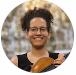 Mulher sorridente com óculos segurando um violino, com fundo desfocado.