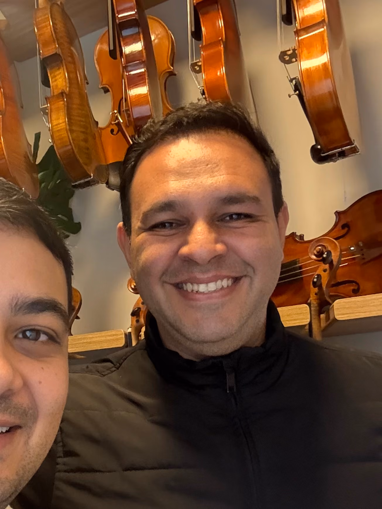 Homem sorrindo com várias violas penduradas na parede atrás dele.