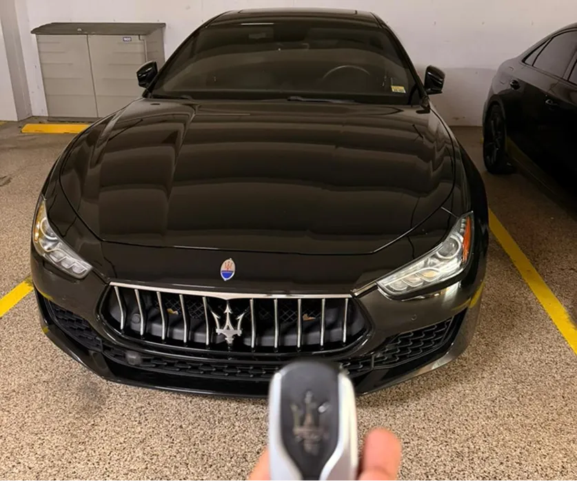 Front view of a black Maserati car parked indoors with a Maserati key fob in the foreground.