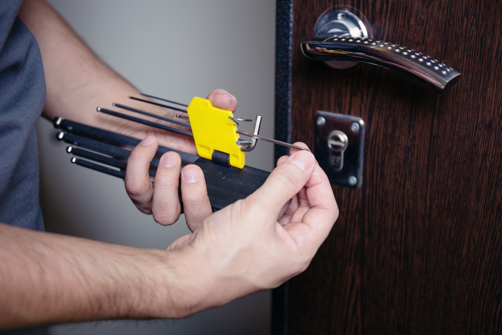 Person holding lock picking tools near a wooden door handle and keyhole.