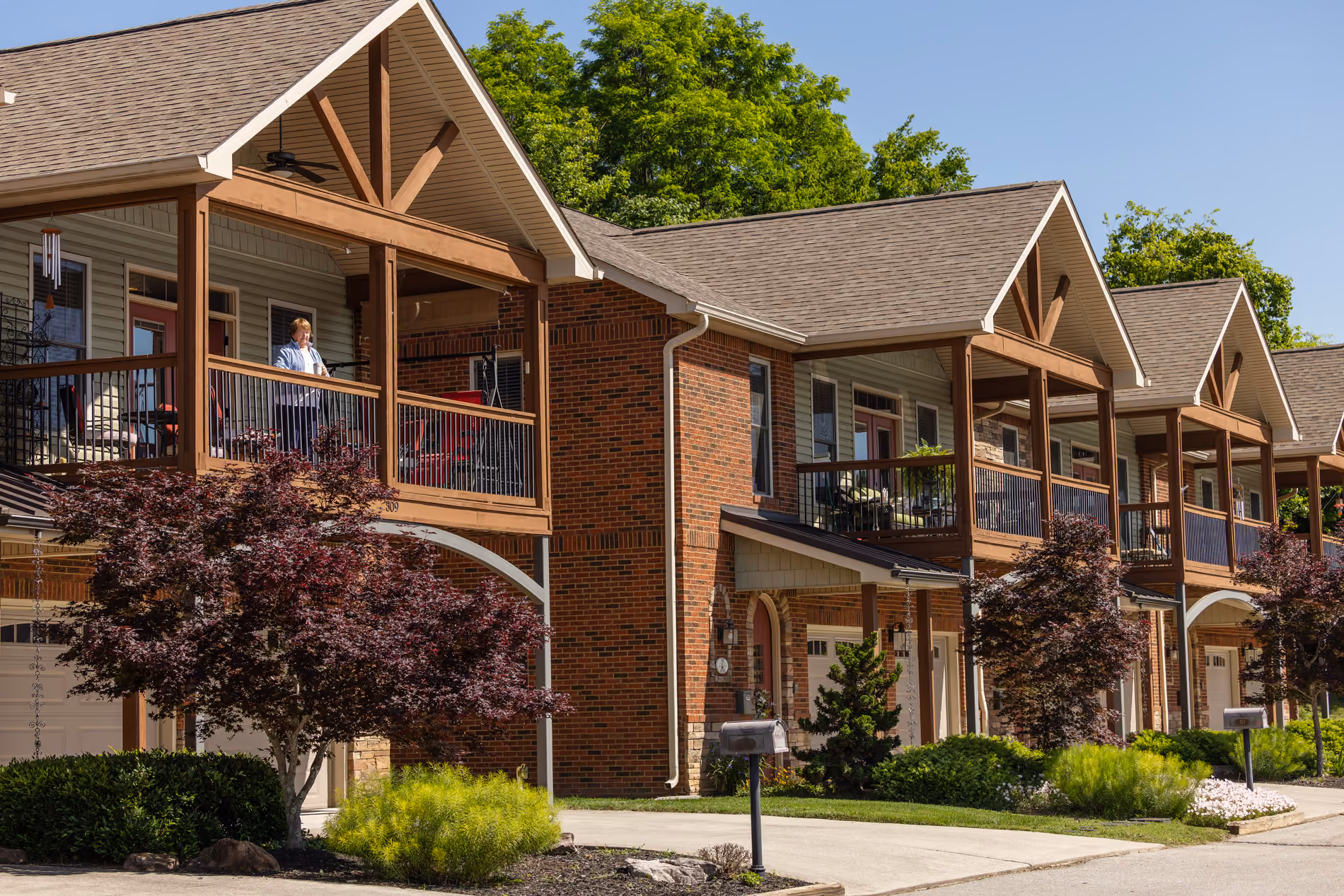 Row of brick townhouses with upper balconies and landscaped yards under a clear sky.