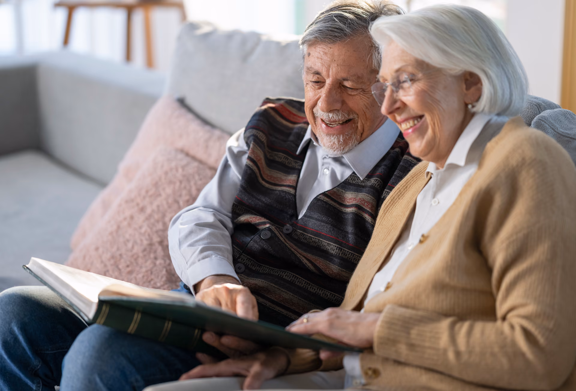Elderly man and woman sitting on a couch happily looking at a photo album together.