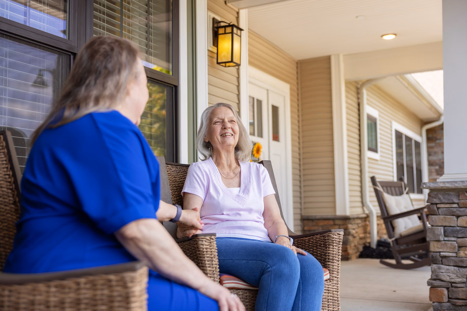 Two women sitting on a porch bench, one smiling and holding hands with the other.