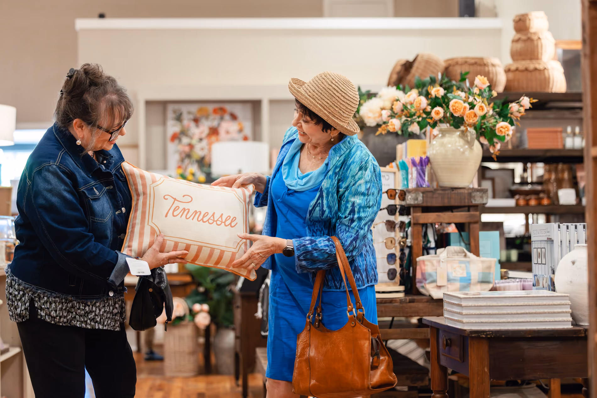 Two women in a store holding a pillow with the word Tennessee on it and smiling.
