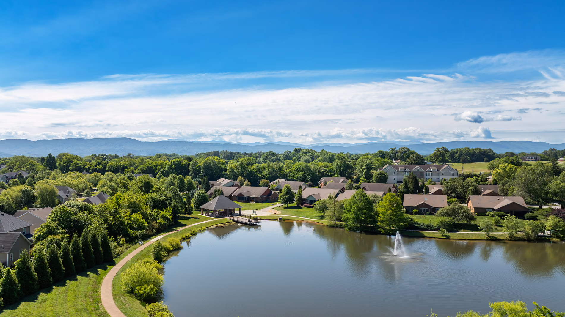 Suburban neighborhood with houses surrounding a pond that has a water fountain and walking path.