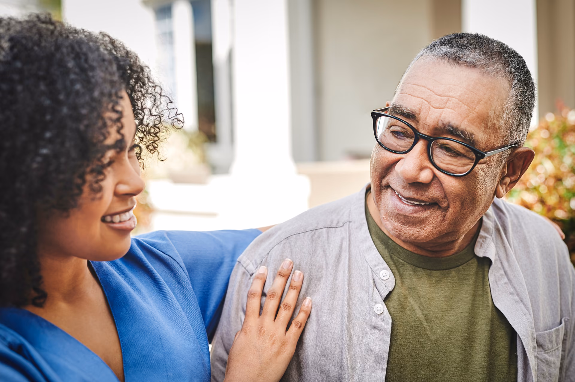 Smiling young woman in blue puts her hand on the shoulder of smiling older man with glasses.