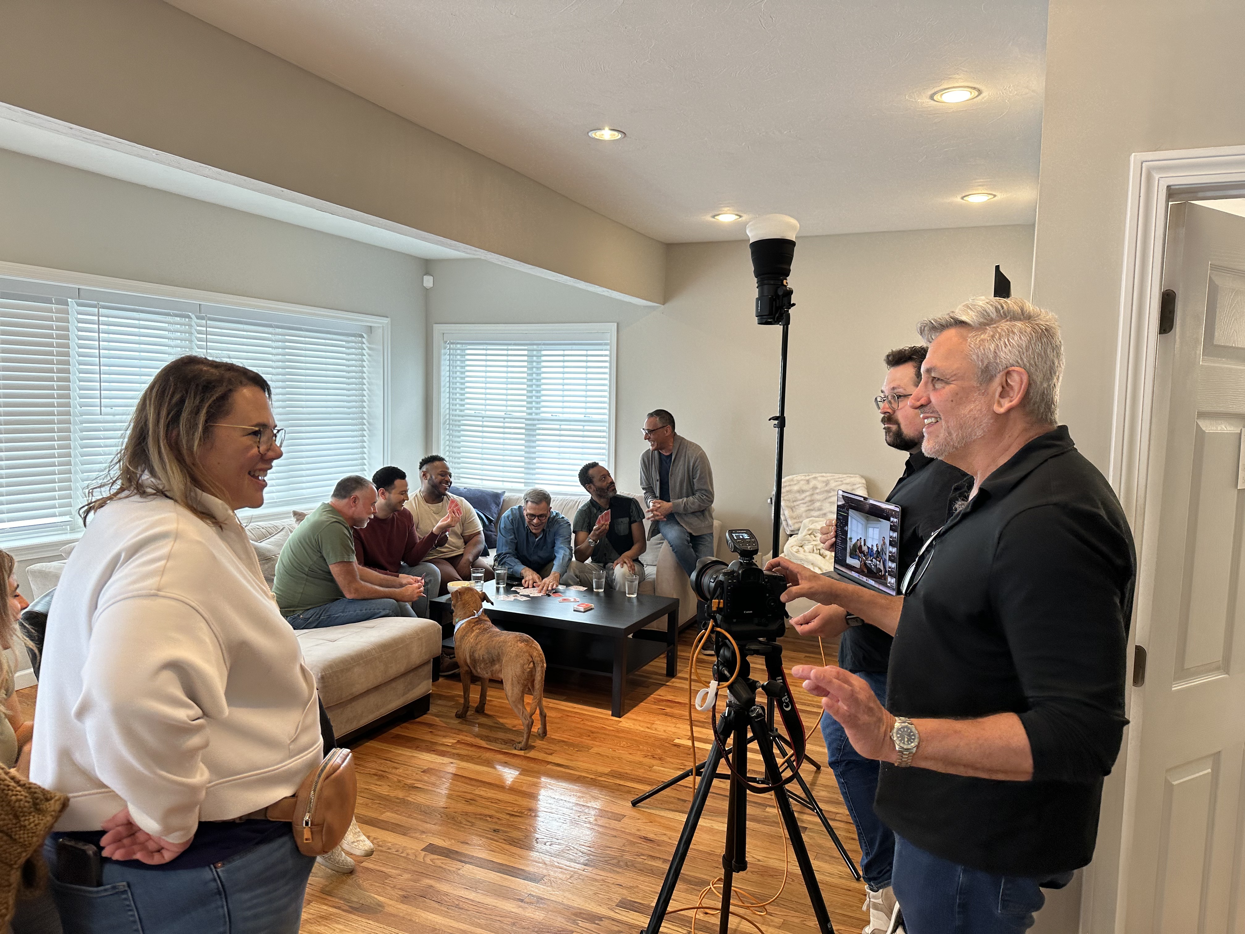 Video shoot in progress in a living room, with a camera on a tripod and people seated on a sofa