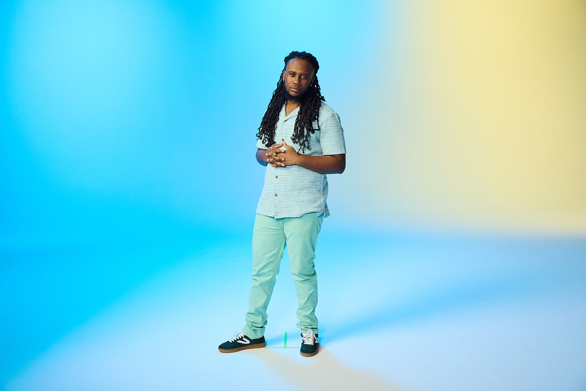 Campaign portrait of a smiling man standing against a soft blue and yellow backdrop