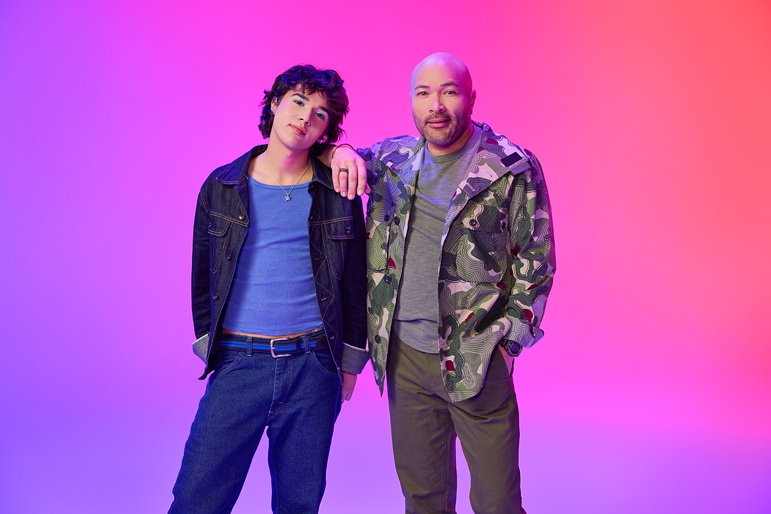 Two people posing together against a purple and pink gradient backdrop