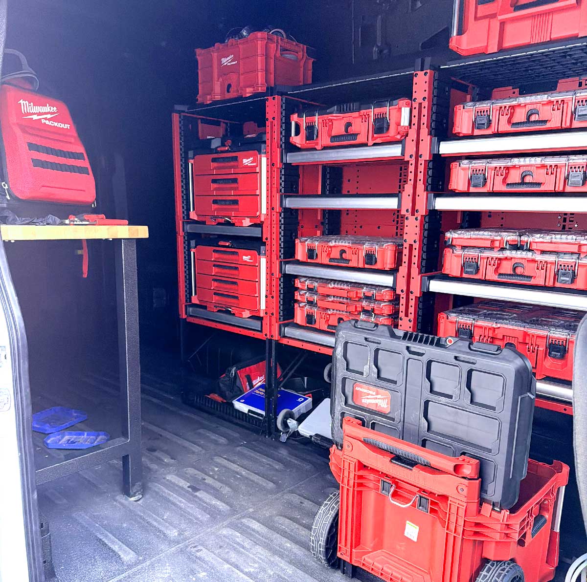 Interior of a van organized with red Milwaukee tool cases and storage shelves.