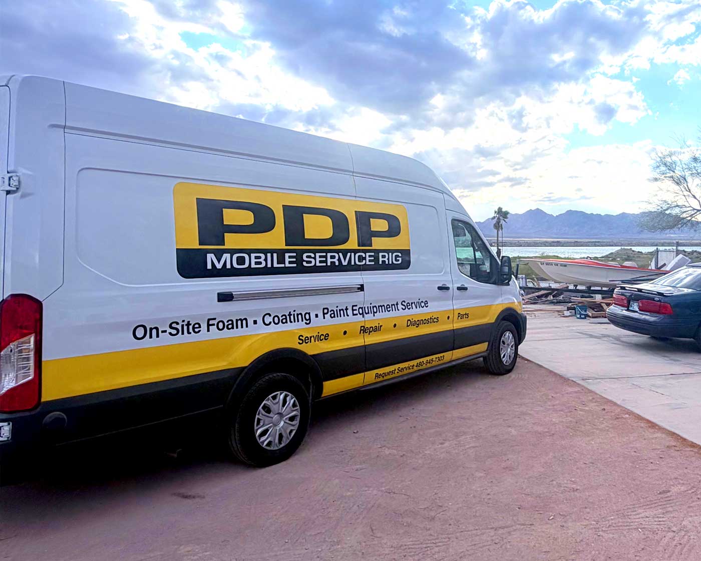 White PDP Mobile Service Rig van with yellow and black stripes parked near a boat and car.
