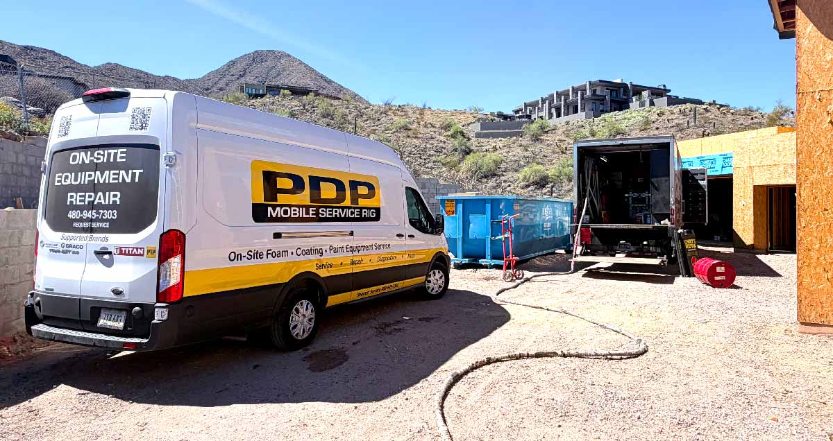 White PDP mobile service van parked by a construction site with mountains and a trailer nearby.