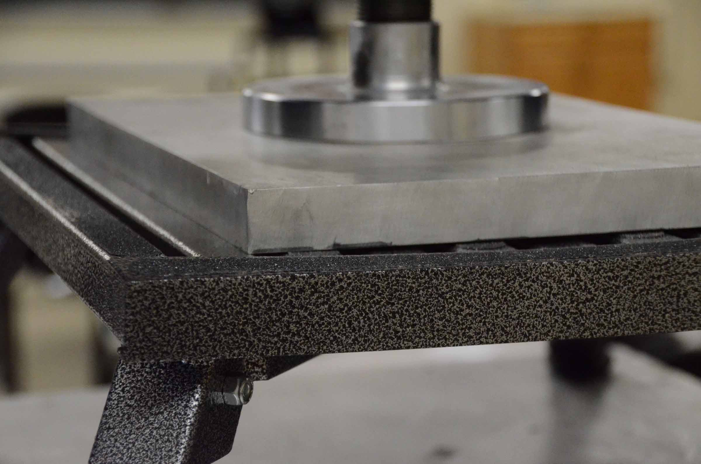 Close-up of a textured metal frame supporting a smooth, flat metal plate with a round metal piece on top.
