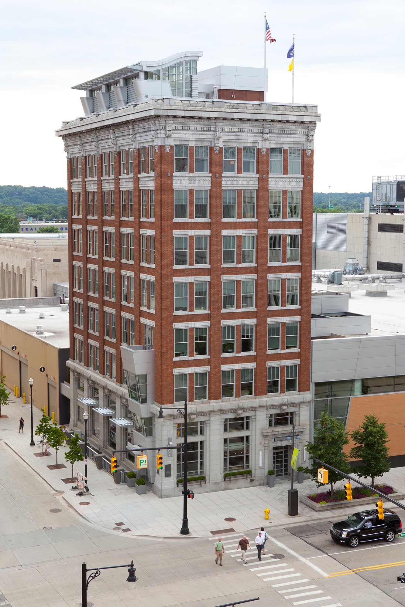Multi-story brick commercial building with large windows at a city street intersection with pedestrians crossing.