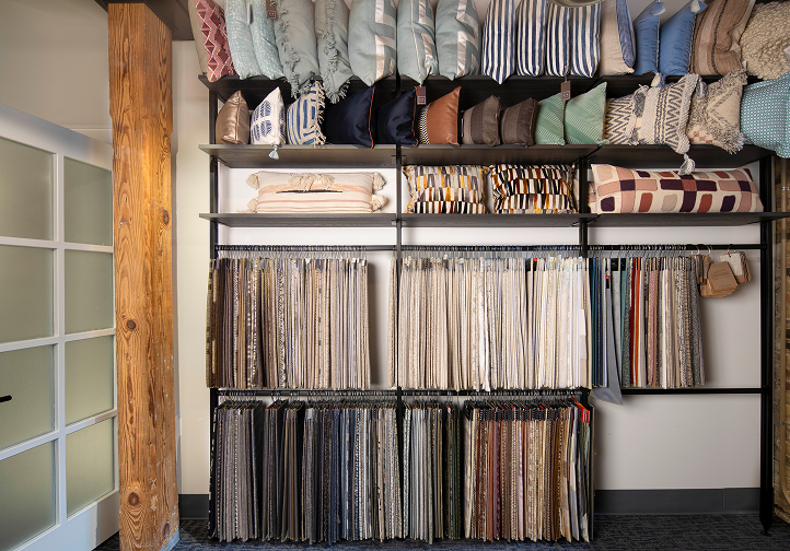 Shelves with folded pillows on top and hanging fabric samples below in various patterns and colors.