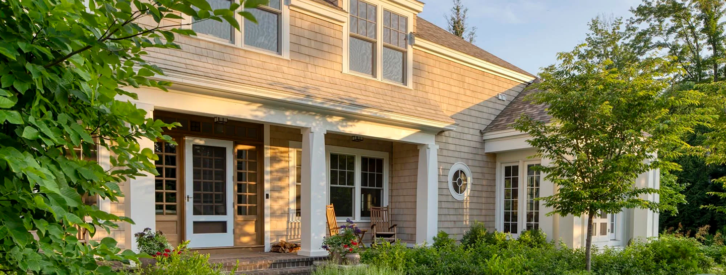 House exterior with wood siding, front porch, rocking chairs, and lush greenery in daylight.