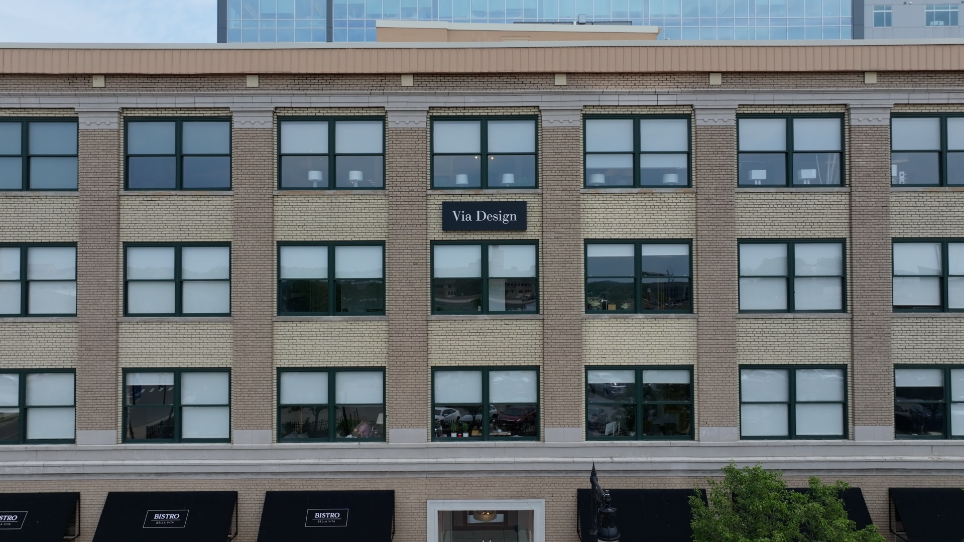 Brick building facade with many windows, Via Design sign in center, and Bistro Bella Vita awnings below.