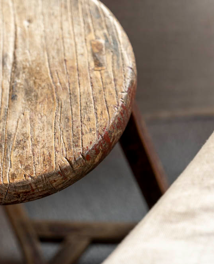 Close-up of a worn, round wooden stool with visible grain and scratches on the seat.