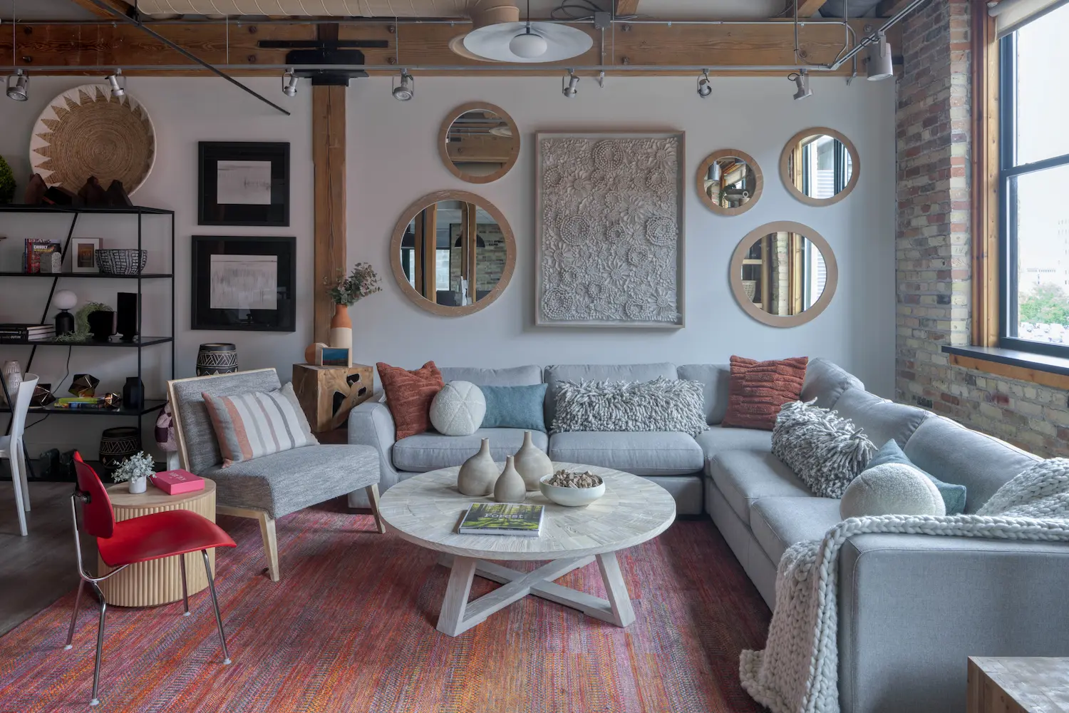Modern living room with gray sectional sofa, round wooden coffee table, circular mirrors, and red chair.