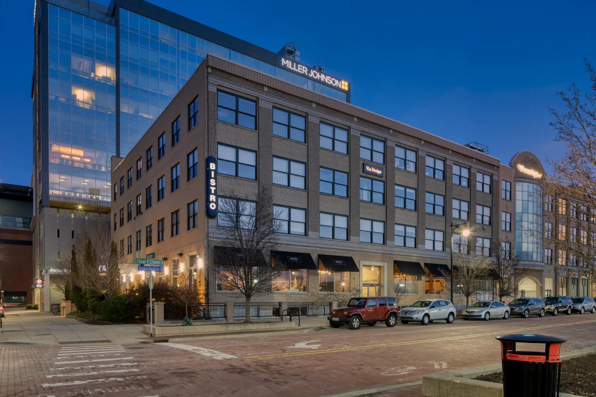 Brick building at dusk with Bistro signage and cars parked along the street in front.