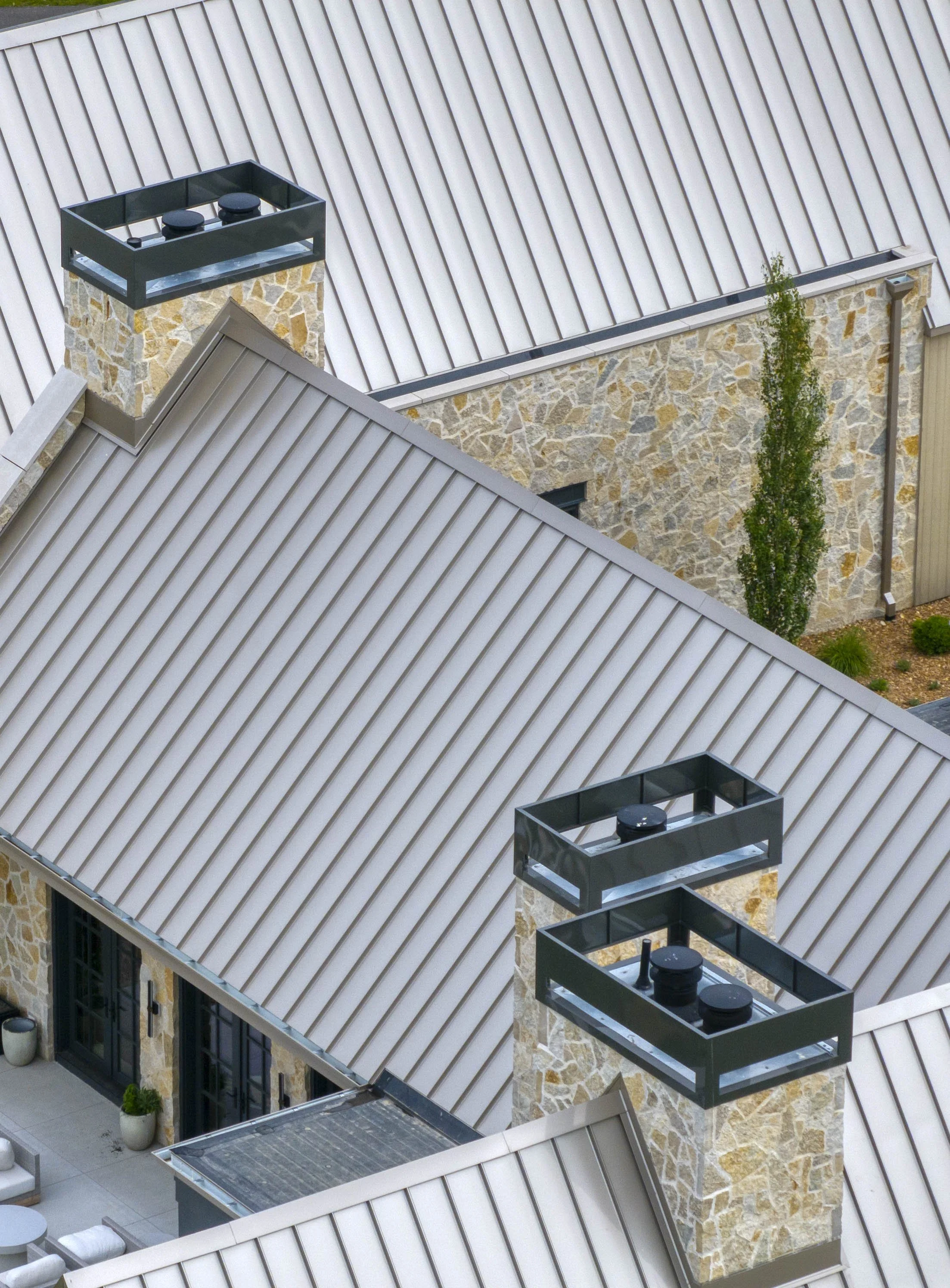 Close-up aerial view of stone chimneys and metal roofs on a modern house with patio below.