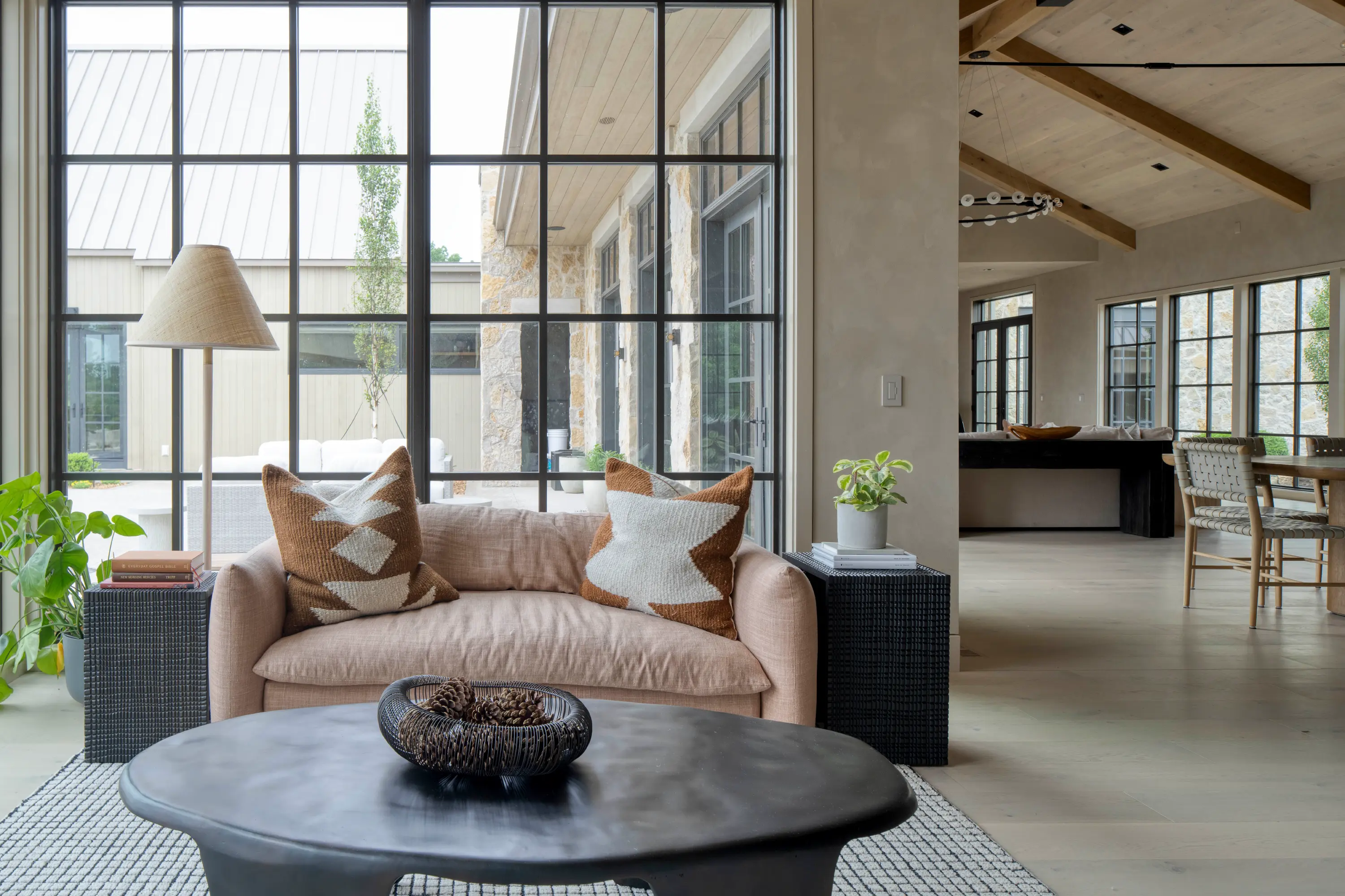 Modern living room with beige sofa, geometric pillows, black coffee table, and large grid window.