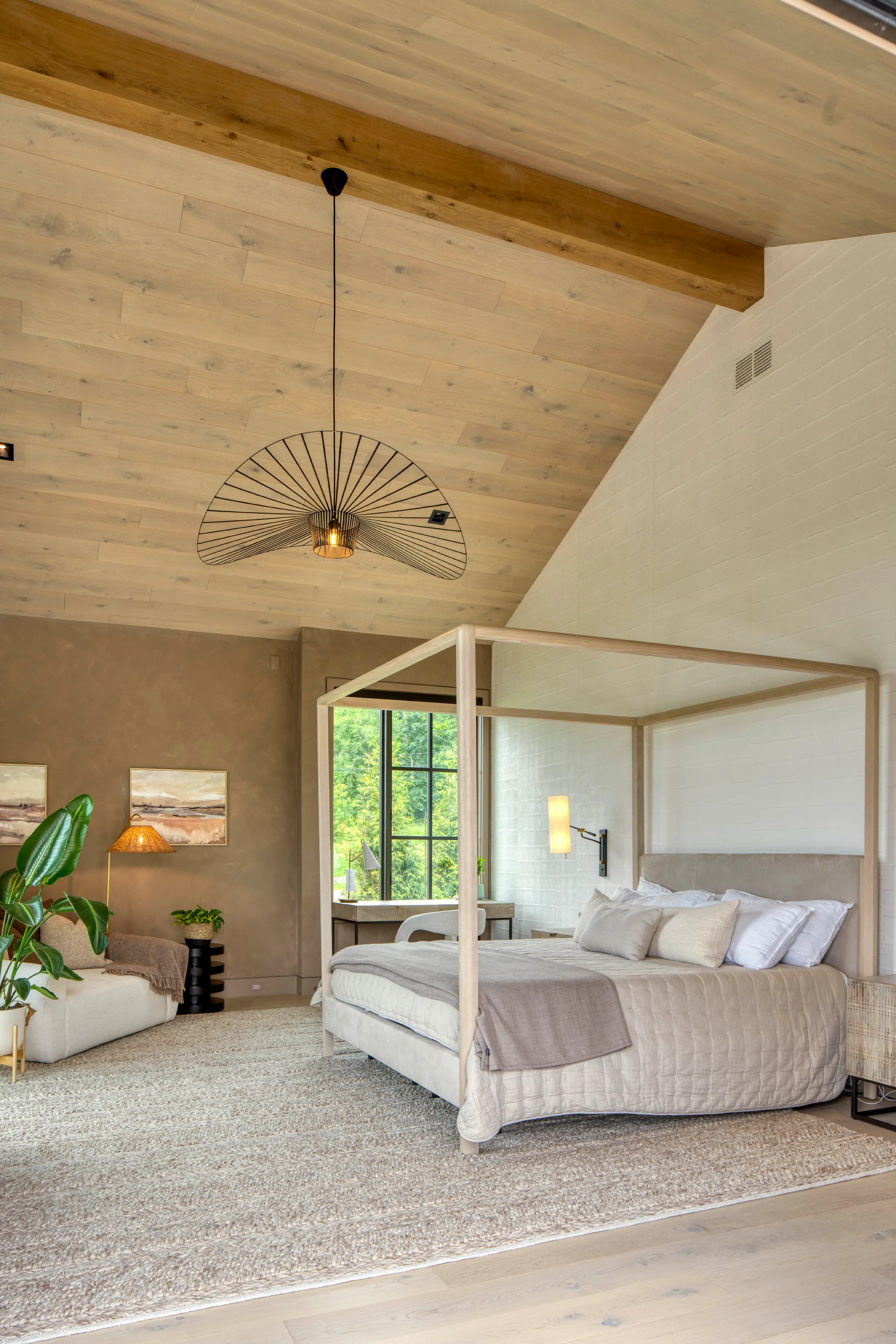 Bright bedroom with light wood four-poster bed, beige bedding, window desk, and modern decor.
